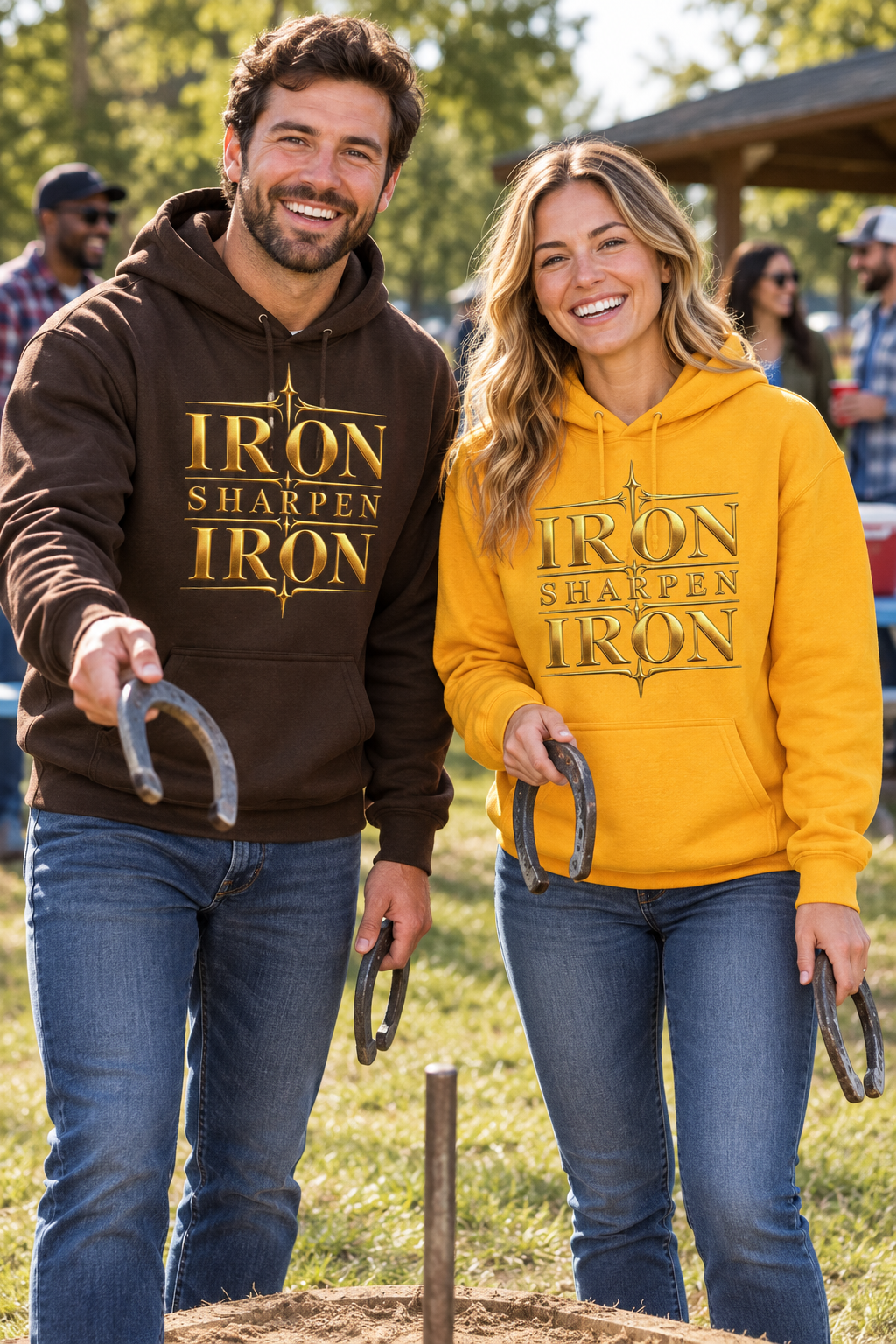 Man in brown and woman in gold Iron Sharpens Iron hoodies playing horseshoes at a church picnic, chest designs visible