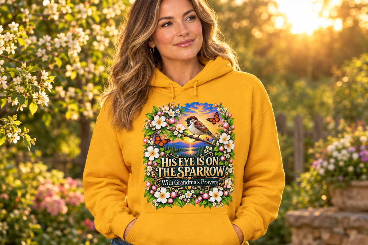 Adult woman wearing the gold His Eye Is on the Sparrow hoodie in a flower garden at golden hour