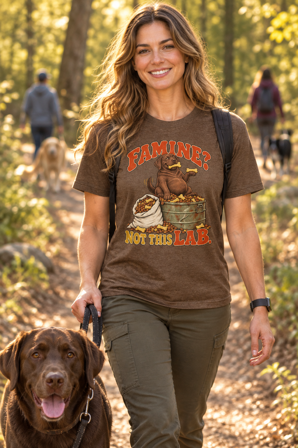 Woman wearing a brown funny chocolate Labrador graphic T-shirt while walking dogs on a wooded trail